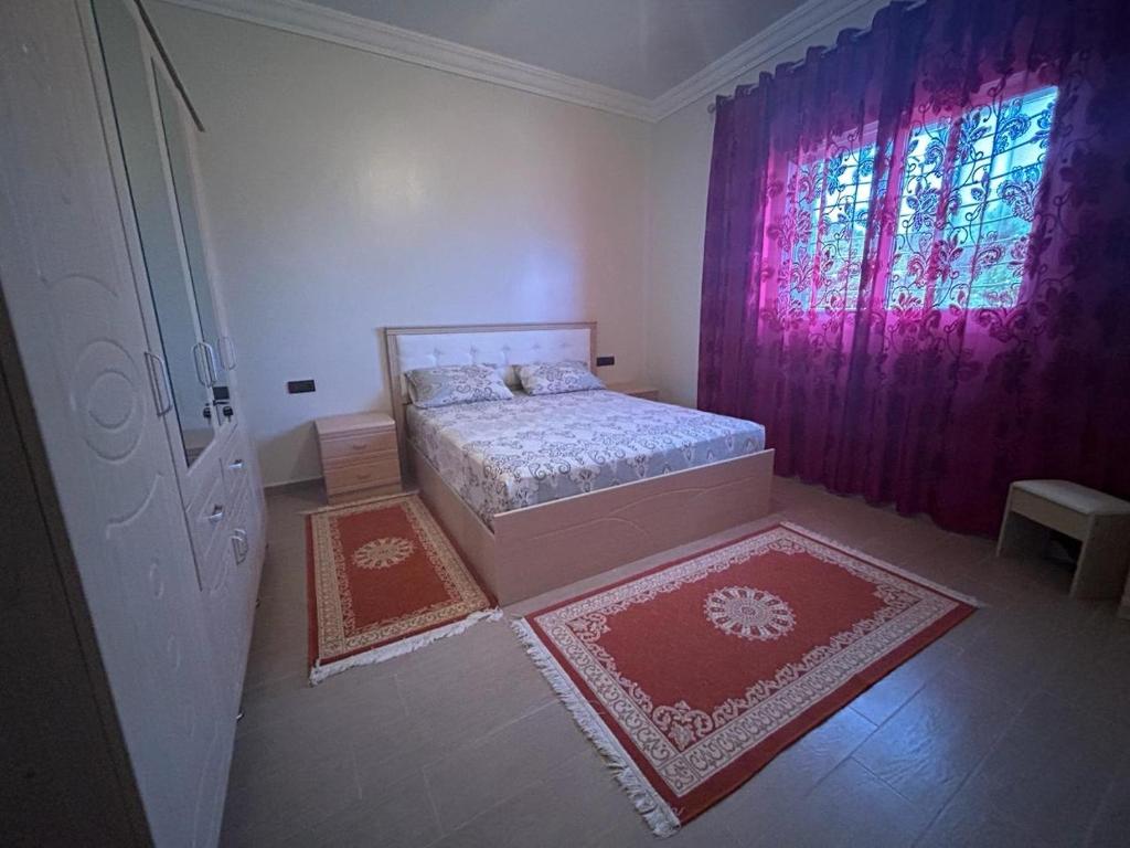 a bedroom with a bed and a window and two rugs at Appartement à Houma, proche Port Tanger Med in Dalia