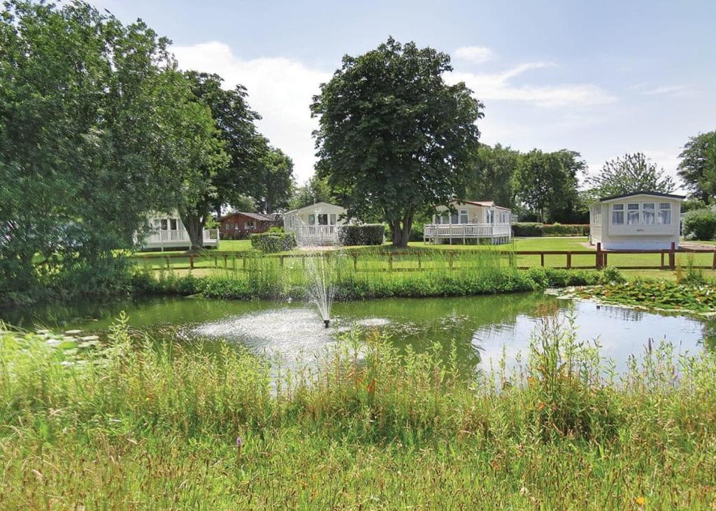 a pond in a field with houses in the background at Fir Trees in Chester