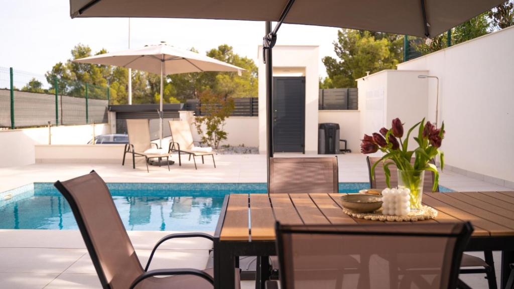 ポロップにあるAmberes apartment, a stylish villa's independent downstairs apartment with private swimming pool and terraceのダイニングテーブル、椅子、パラソル、プールが備わります。