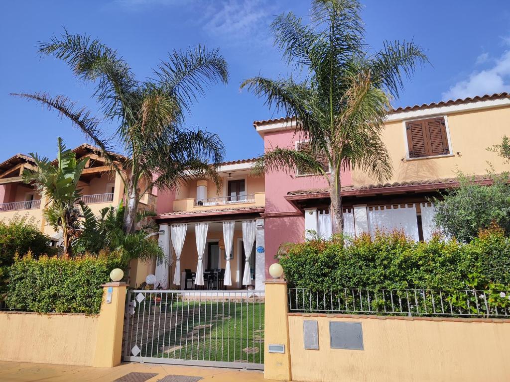 una casa rosa con palmeras y una valla en Villasimius Villa Agorà, en Villasimius