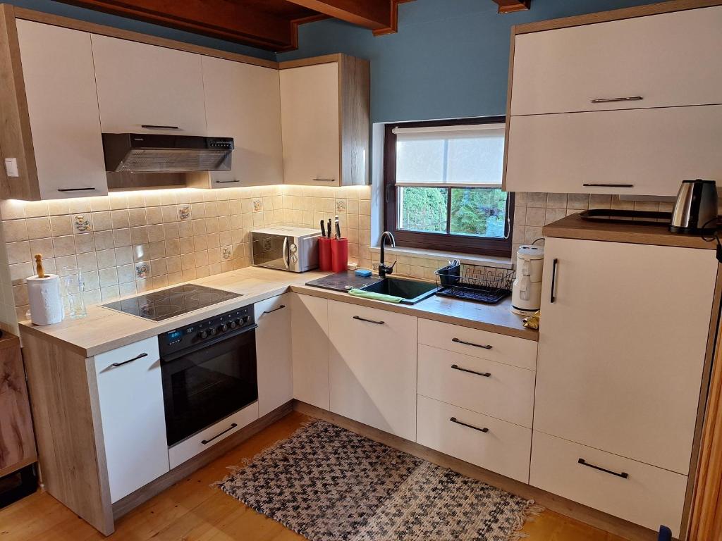 a kitchen with white cabinets and a sink and a window at Domek pod lasem w miejscowości Rozogi- Mazury in Rozogi
