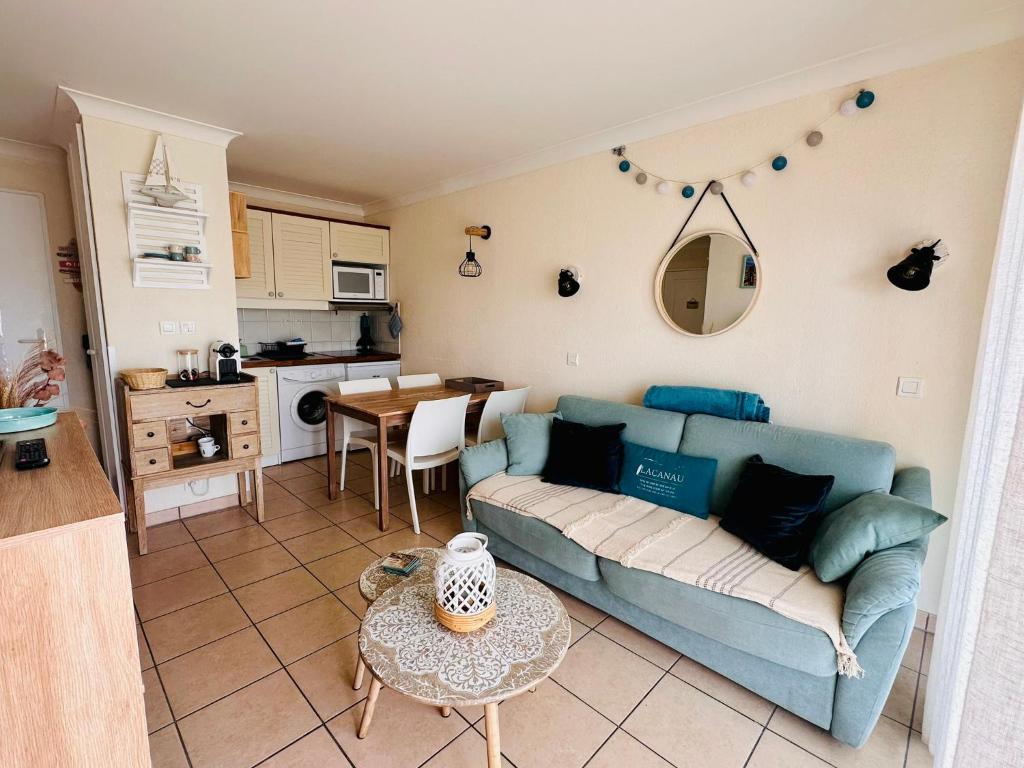 a living room with a blue couch and a kitchen at Appartement rez-de-chaussée entre dunes et ocean in Lacanau-Océan