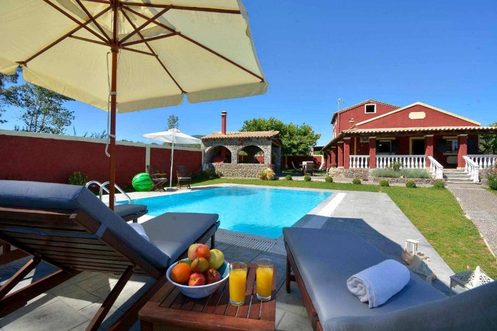 una piscina con una mesa con un bol de fruta y una sombrilla en Pavlos Sofia Villa, en Corfú