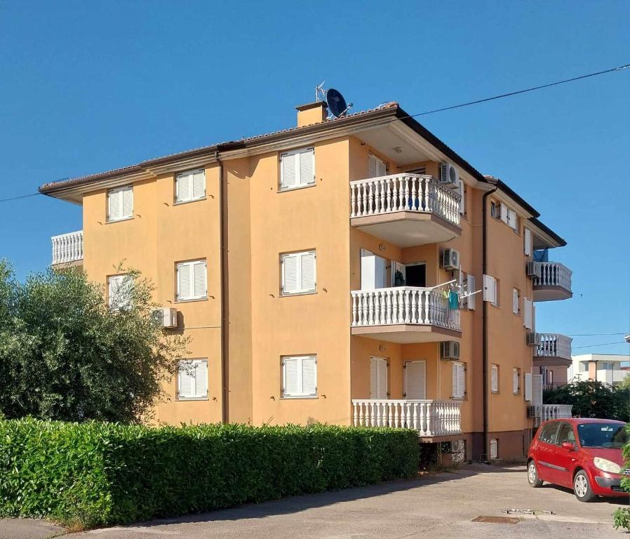 un edificio amarillo con balcones y un coche rojo aparcado delante en ULA LA apartment, en Umag