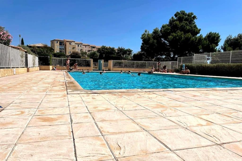 une grande piscine avec des personnes assises autour de celle-ci dans l'établissement St-Pierre-La-Mer, bel appartement a dans residence avec piscine et tennis entre 5 et 10 min de la plage, à Fleury
