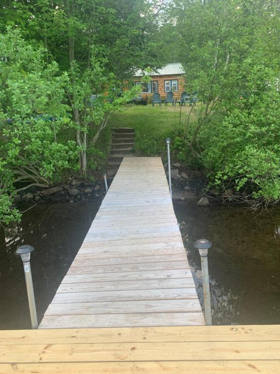 a wooden bridge over a river with a house in the background at Adirondack Waterfront Cabin Upper Hudson Tributary in Lake Luzerne