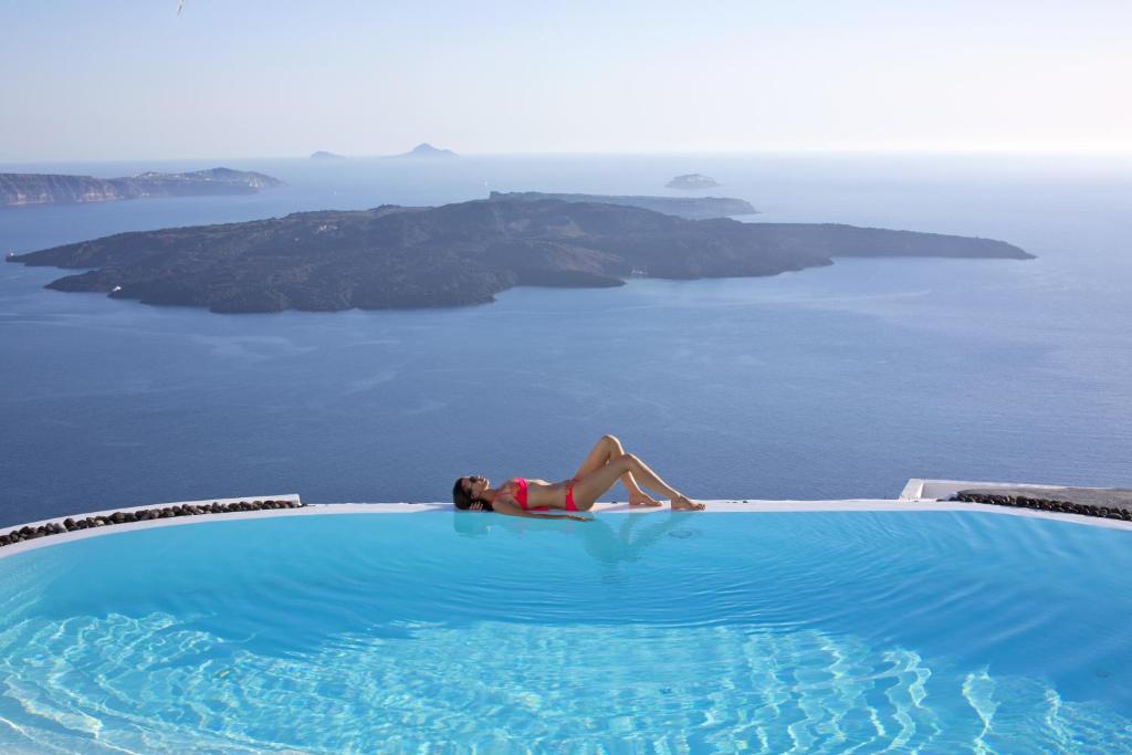 a woman laying in a swimming pool next to the ocean at Alta Vista Suites in Firostefani