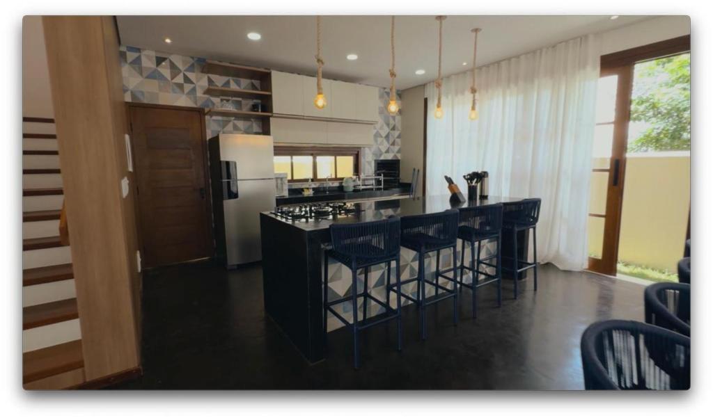 a kitchen with a bar with chairs and a refrigerator at Casa Aconchego - Barreirinhas in Barreirinhas