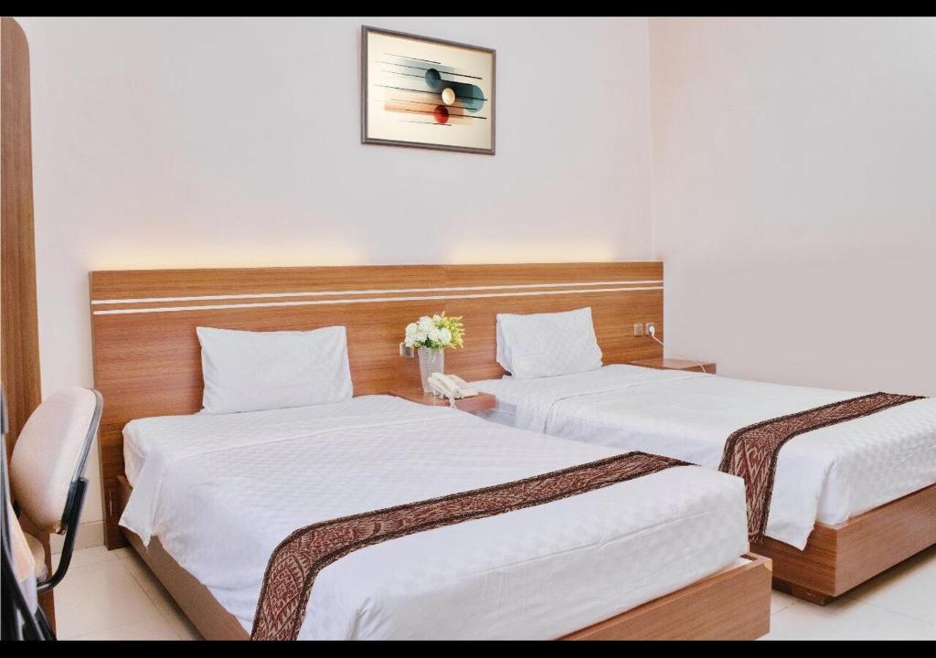 two beds in a hotel room with white sheets at Gapura Residence Airport Semarang by Sinergi in Semarang