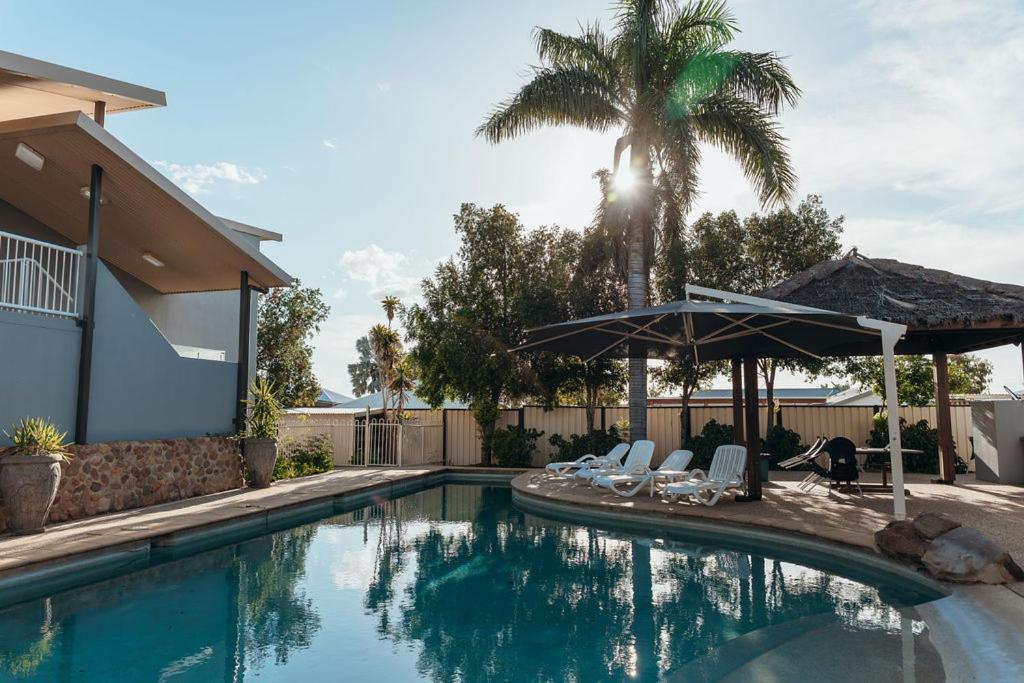 einen Pool mit Stühlen, einem Sonnenschirm und einer Palme in der Unterkunft The Mayfair Ridge Hotel in Emerald