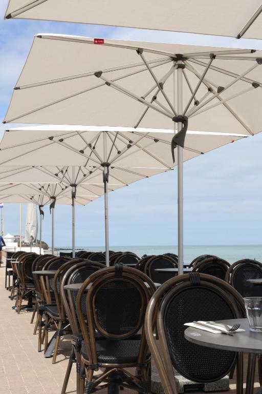 una fila de mesas y sillas con sombrillas blancas en Le Clos Normand en Saint-Aubin-sur-Mer