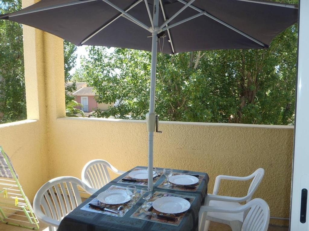 - une table avec un parasol et des chaises blanches dans l'établissement APPT 3 PCES MEZ 45m2 + TERRASSE 7m2 REF 4007, à Le Castellas