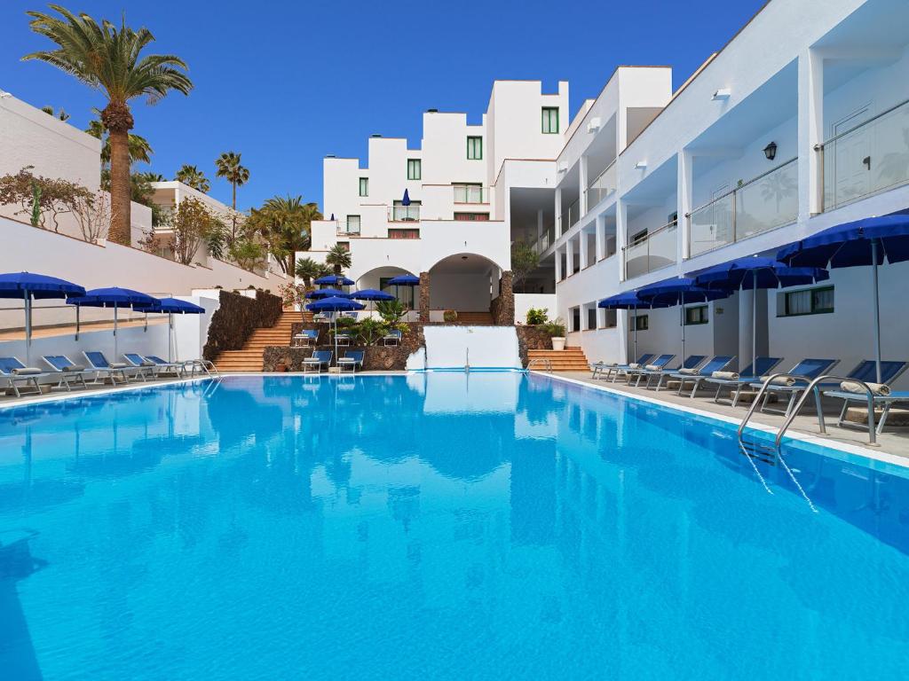 a swimming pool with blue water in front of a building at Aparthotel Esquinzo Y Monte Del Mar in Playa Jandia