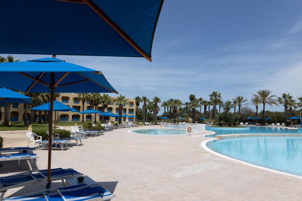 una piscina en el complejo con sillas y sombrillas en Ramada Plaza by Wyndham Tunis, en Gammarth