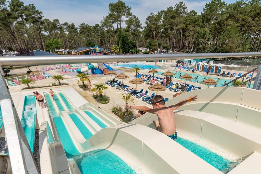 - un garçon sautant sur un toboggan aquatique à la piscine dans l'établissement MH 395 3 chambres et 1 salle de bain dans camping 4 étoiles, à Saint-Julien-en-Born