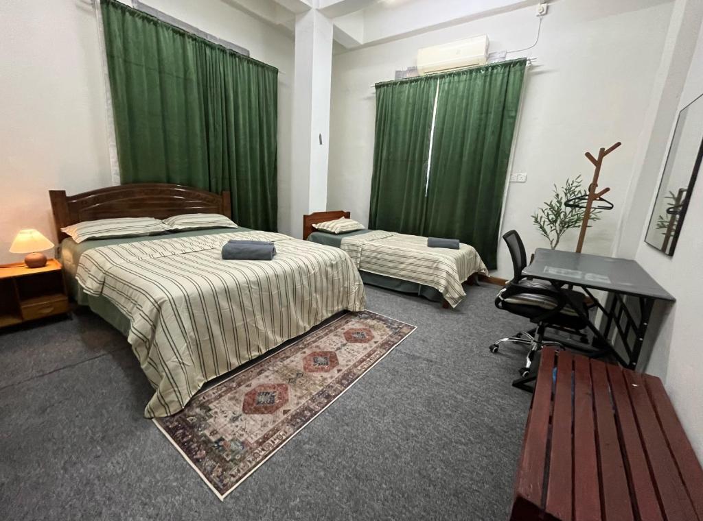 a bedroom with two beds with green curtains and a desk at La Wood Homestay near Kuala Besut Jetty in Kuala Besut