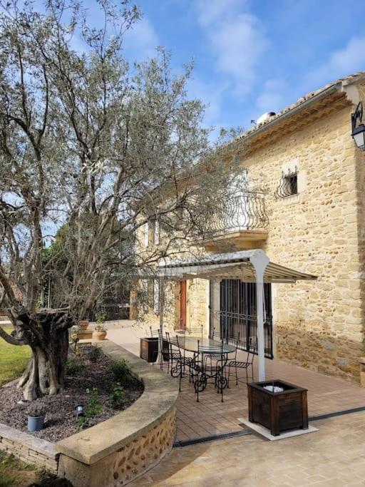 une terrasse avec une table et un arbre en face d'un bâtiment dans l'établissement Le Mas de l Olivier, à Saint-Geniès-de-Comolas