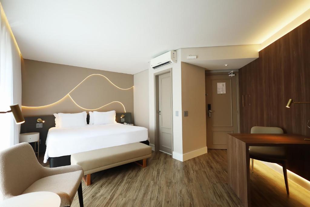 um quarto de hotel com uma cama branca e uma secretária em Radisson Oscar Freire em São Paulo