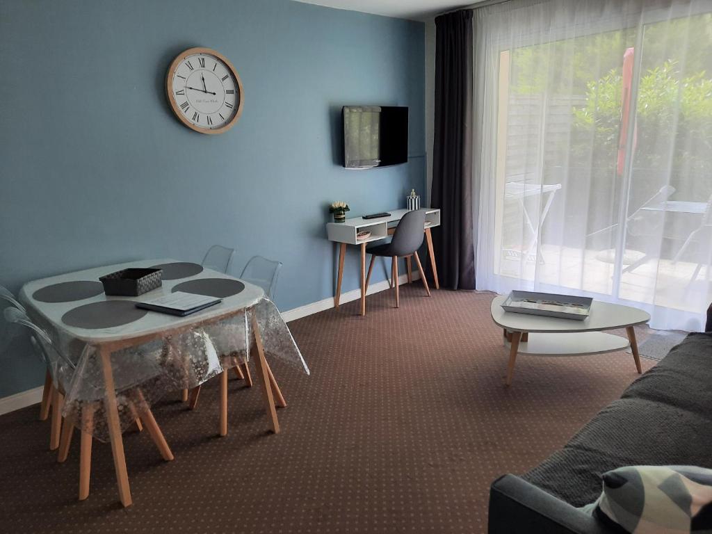 ein Wohnzimmer mit einem Tisch und einer Uhr an der Wand in der Unterkunft Appartement AB DU PARC in Neufchâtel-Hardelot