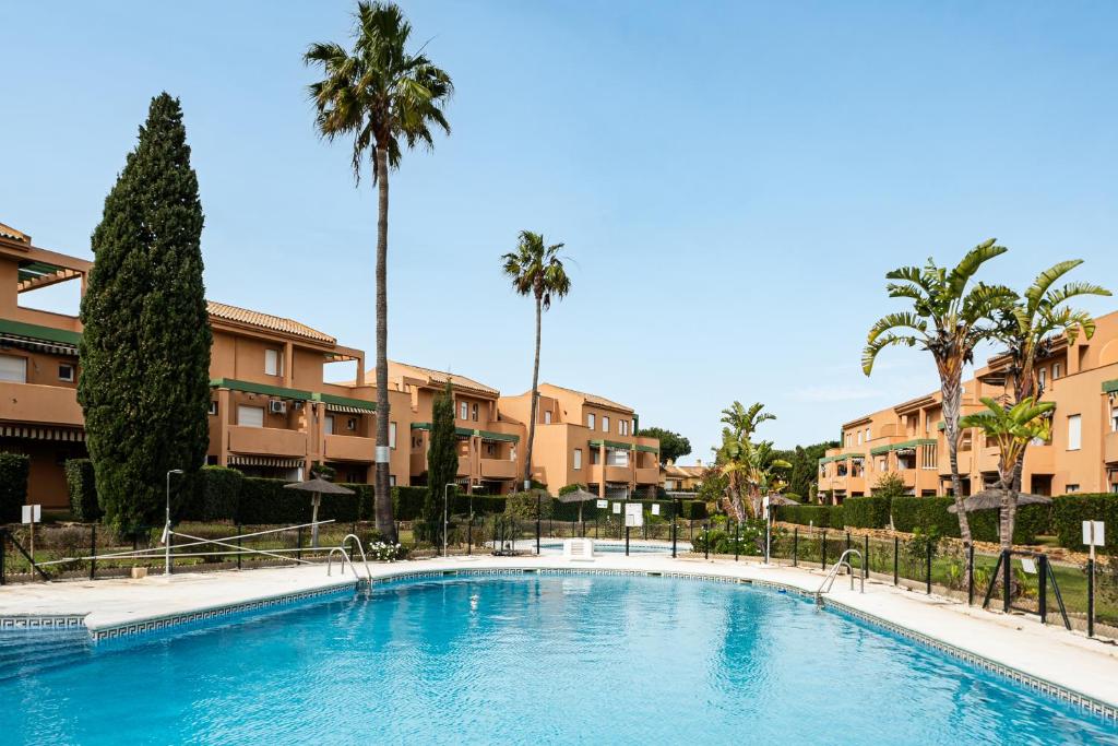 ein großer Swimmingpool mit Palmen und Gebäuden in der Unterkunft Jardín del Golf apartamento con jardín privado in Chiclana de la Frontera