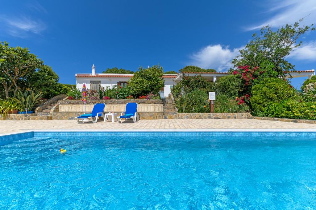 a swimming pool with two blue chairs and a house at Bela casa na Costa Vicentina in Aljezur