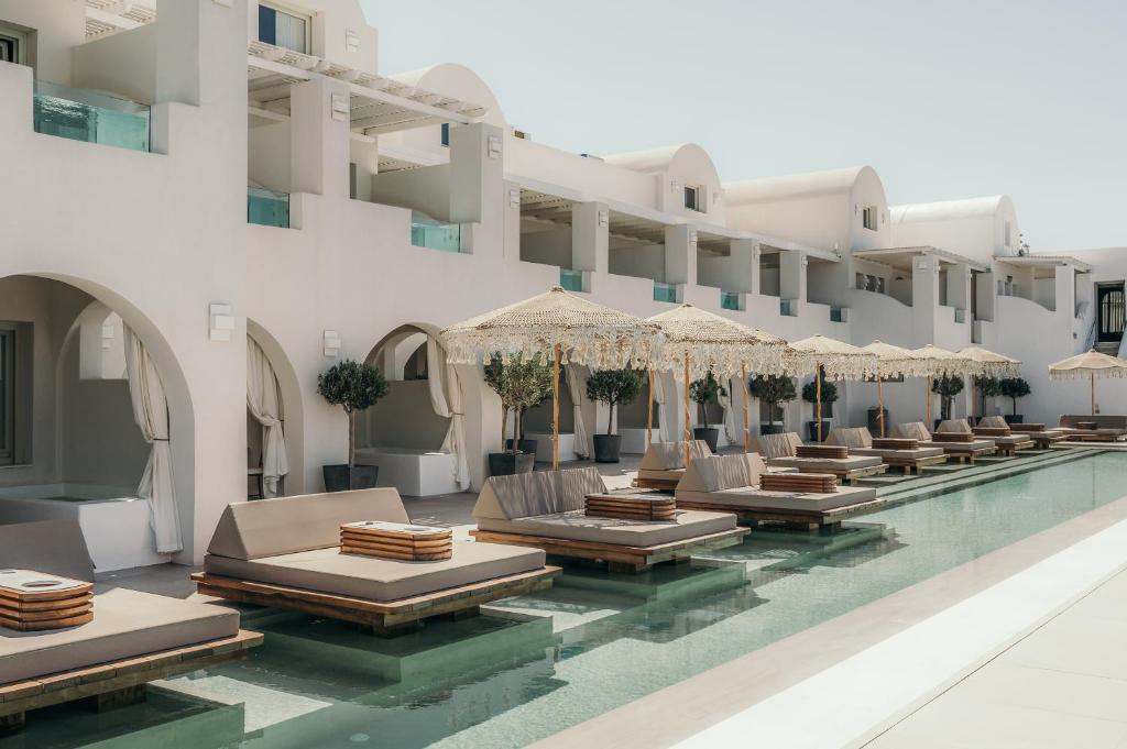 Apeiron Blue Santorini - Sustainable Adults Only 14 Plus في فيرا: مسبح الفندق مع كراسي الصالة والمظلات