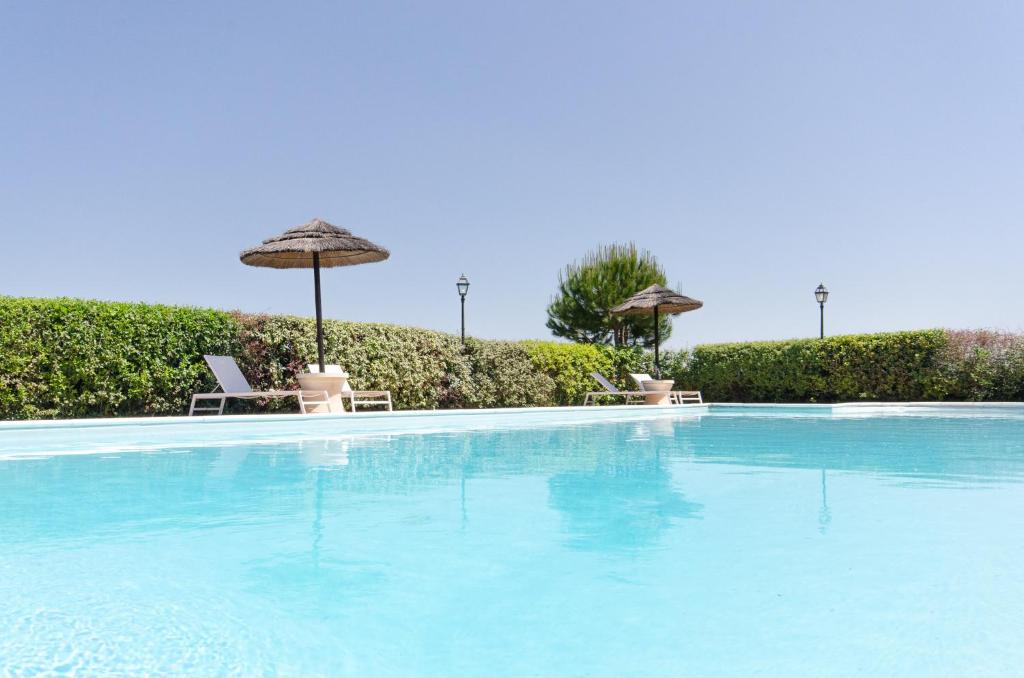a large swimming pool with two umbrellas and two chairs at Agriturismo Ca'de'Gatti in Faenza