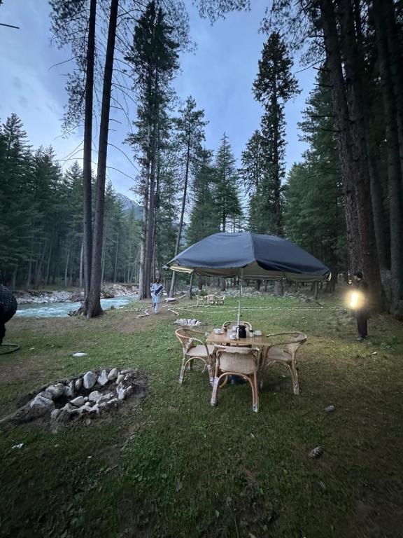 a picnic table with a blue umbrella in a field at Infinity Villa and Resort Kumrat Valley in Tāl