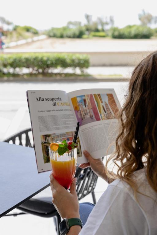 a woman reading a magazine and holding a drink at Hotel Continental in Caorle