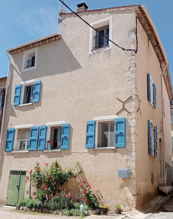 un bâtiment avec des fenêtres bleues et des fleurs devant lui dans l'établissement La retapée, à Quinson