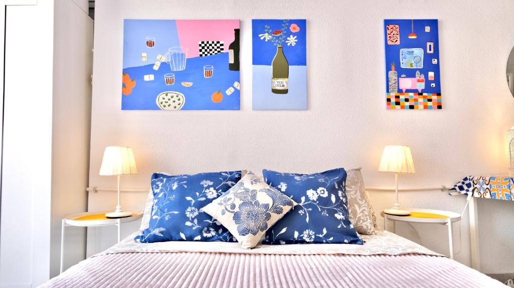 a bedroom with a bed with blue pillows and paintings at White studio in Torrevieja