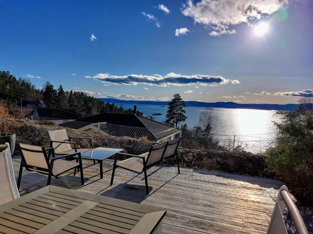 Flaskebekk at Nesodden with unbeatable Oslo Fjord views and a private beach hut في Nesoddtangen: سطح مع طاولة وكراسي وإطلالة على البحيرة