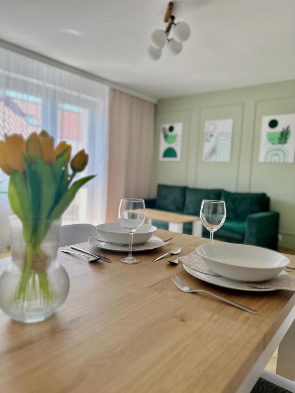 a table with plates and glasses and a vase with flowers at Apartament Zielone Serce Miasta in Mrągowo