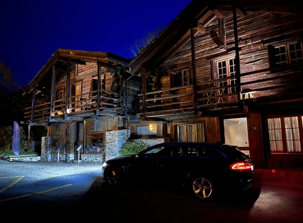 ein schwarzes Auto, das vor einem Holzgebäude parkt in der Unterkunft Mazot Agora Suite - Pop-Up Gallery Experience Suite in Salvan