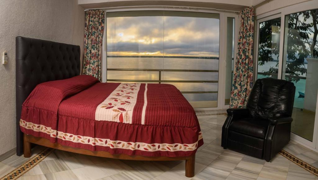 um quarto com uma cama, uma cadeira e uma janela em Casa Bacalar em Bacalar