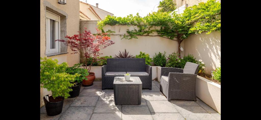 eine Terrasse mit Korbstühlen, einem Tisch und Pflanzen in der Unterkunft Maison avec cheminée et jardin près des commerces in Béziers