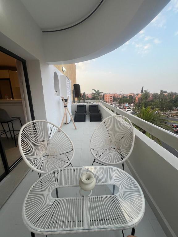 Un balcón con 2 sillas blancas y una mesa. en Appartement dans triangle d’or en Marrakech