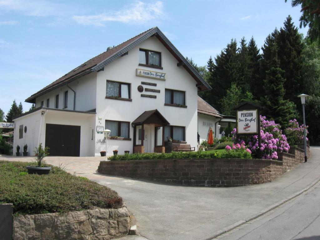 une maison blanche avec des fleurs devant elle dans l'établissement Pension - Der Berghof, à Braunlage
