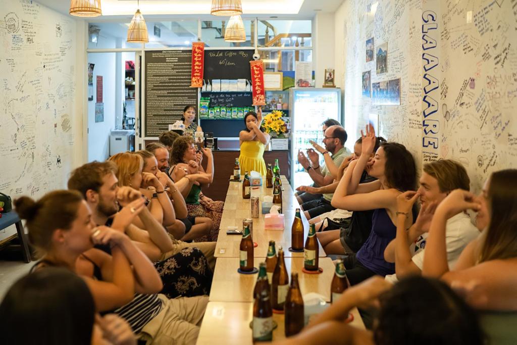um grupo de pessoas sentadas em torno de uma longa mesa com garrafas em Hoi An Love.Ly Hostel em Hoi An