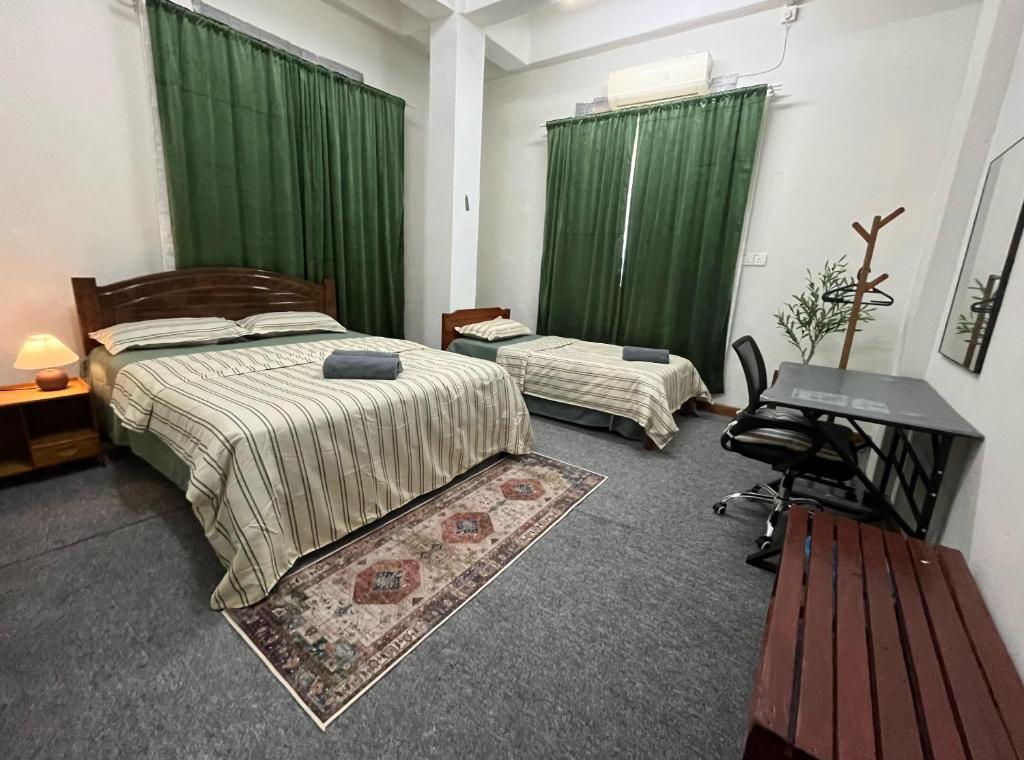 a bedroom with two beds with green curtains and a desk at La wood homestay in Kuala Besut