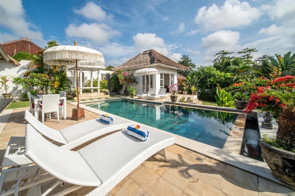 a pool with chairs and an umbrella next to a house at Villa Moana Poe Uluwatu in Uluwatu