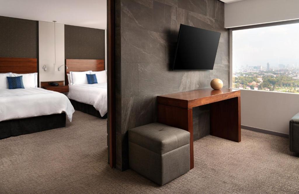 A compact in-room desk beside a window, with twin beds visible beyond.