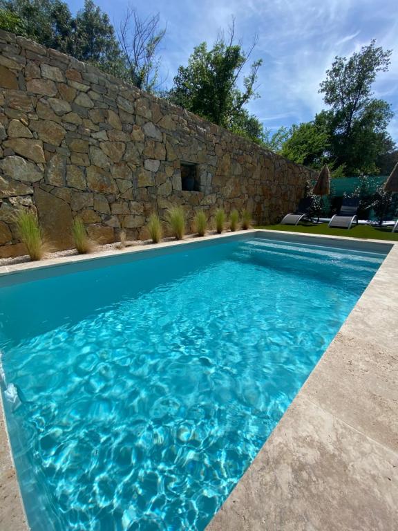 une piscine d'eau bleue et un mur en pierre dans l'établissement Villa neuve - piscine chauffée, à Lorgues