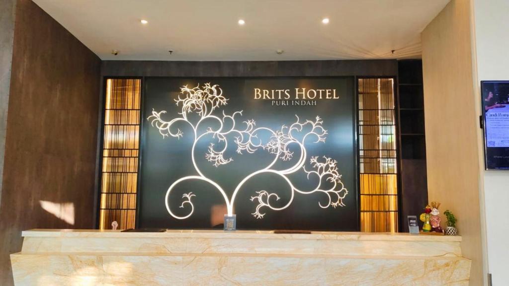 a sign for a hotel with a tree on the wall at Brits Hotel Puri Indah in Jakarta