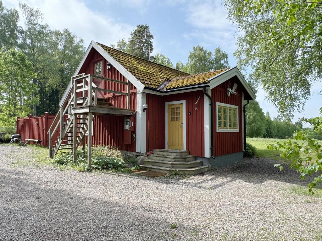 Historic wilderness cabin near Tystberga في Tystberga: منزل صغير احمر مع باب اصفر وسلم