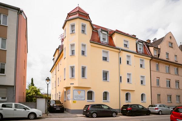 a large yellow building with cars parked in front of it at Boardinghouse Victory in Augsburg