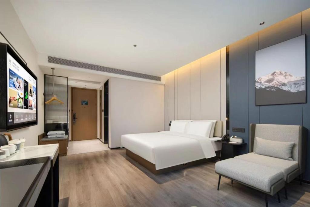a bedroom with a bed and a chair and a television at Atour Hotel Jiaxing Haiyan Economic Development Zone in Jiaxing