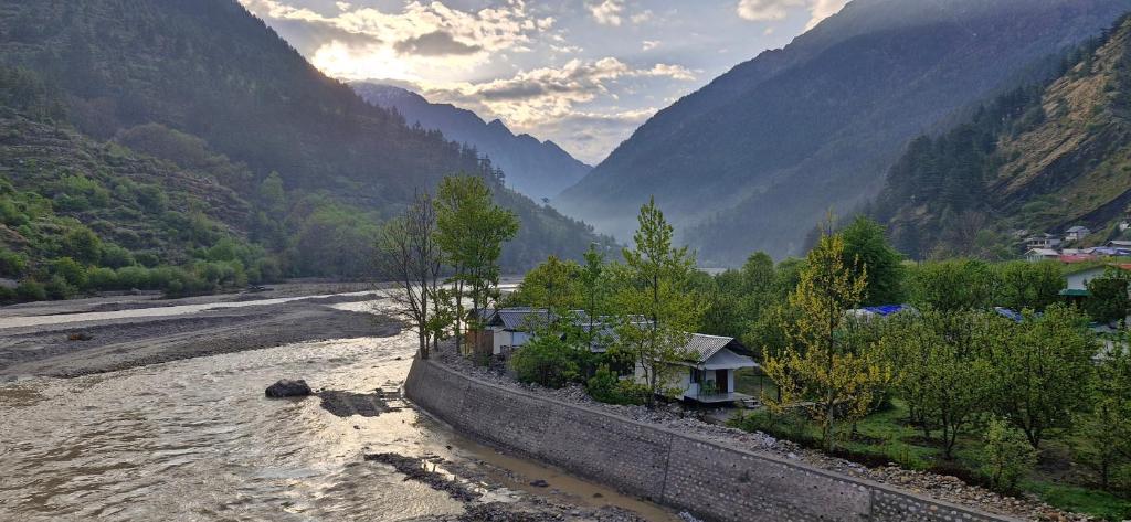 una casa accanto a un fiume con montagne sullo sfondo di Hinwali Kanthi River Side Camp and Cottage a Harsil