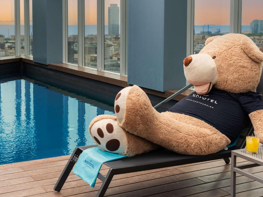 ein großer Teddybär auf einer Bank neben einem Pool in der Unterkunft Novotel Barcelona City in Barcelona