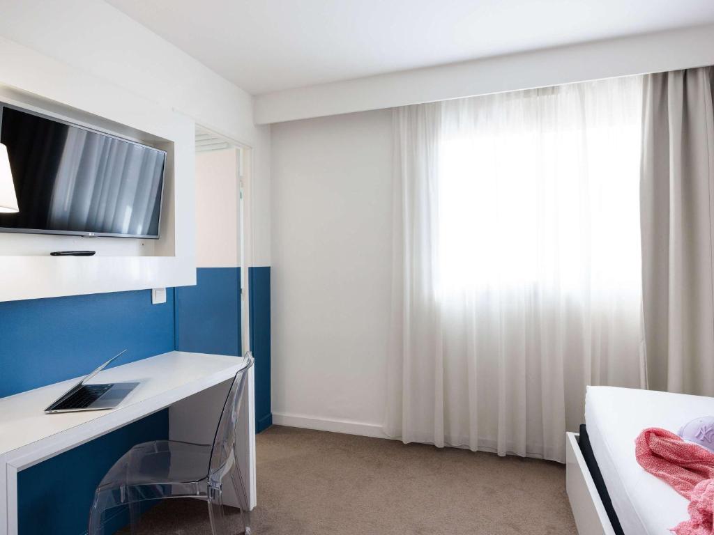 a bedroom with a desk and a tv on the wall at Ibis Styles Menton Centre in Menton